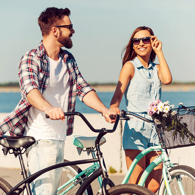 They love the active life. Happy young couple rolling their bicycles and looking at each other with smileswhile walking outdoors